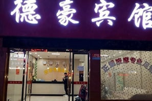 L’entrée d’un hôtel, avec un panneau lumineux au néon, un comptoir d’accueil et un espace d’attente bien visible.