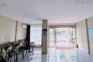 A hotel lobby with a reception desk, seating area, and a glass door entrance.