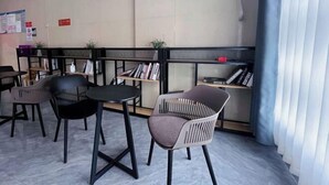 A modern waiting area with black and grey chairs, a small table, and a bookshelf with books and a phone.