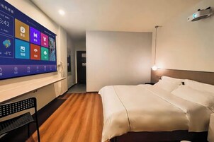 Habitación de hotel con cama, escritorio y una pantalla grande que muestra información de la estancia.