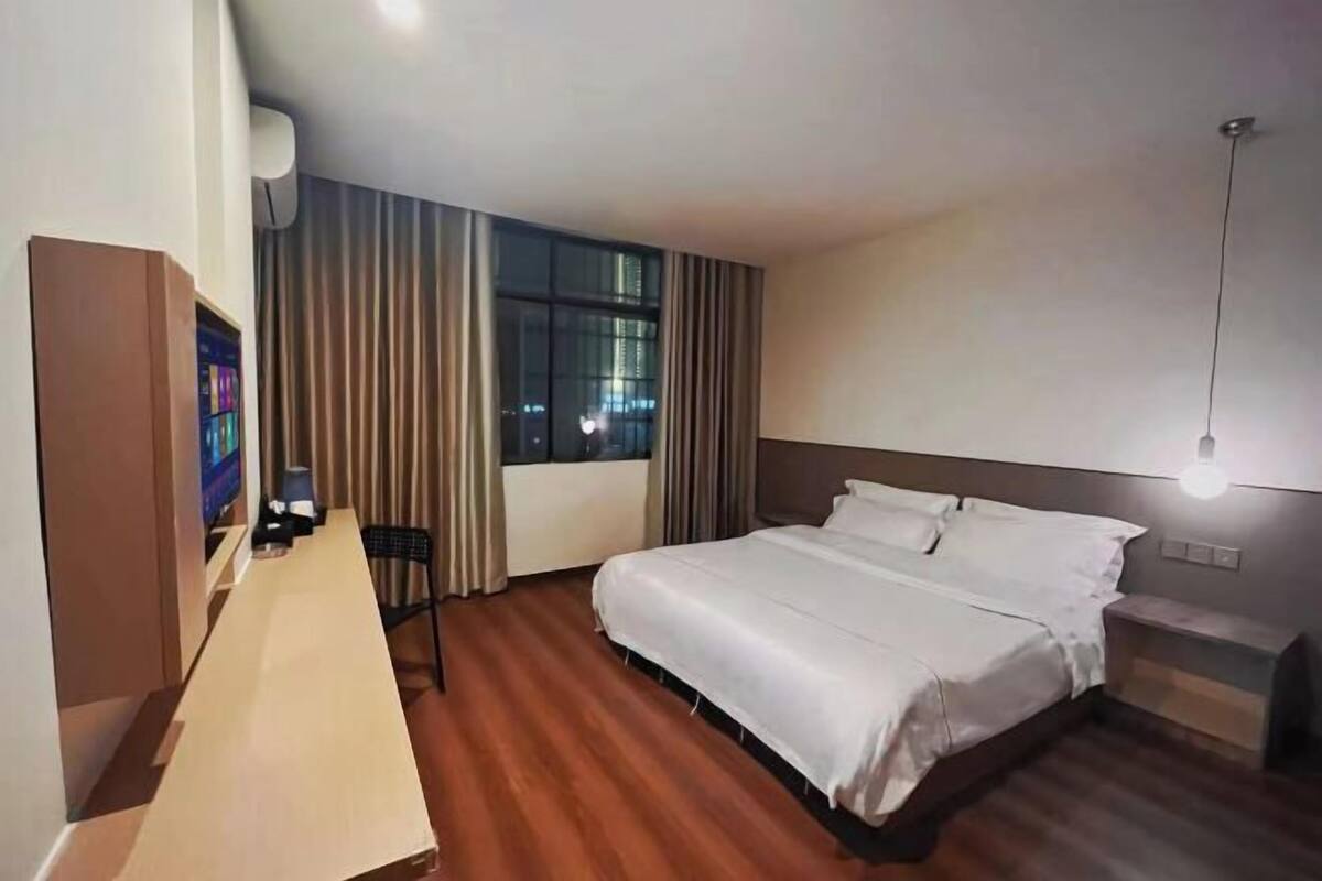 Quarto de hotel com uma cama, uma mesa com cadeira, uma televisão e uma janela com cortinas.