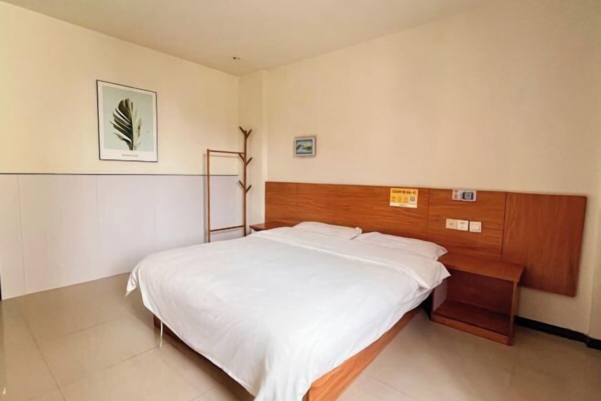 Un lit bien fait dans une chambre d’hôtel, avec une tête de lit en bois, une petite table de chevet et un cadre photo fixé au mur.