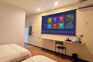 Habitación de hotel con una gran pantalla digital en la pared, un escritorio pequeño con una silla y dos camas.