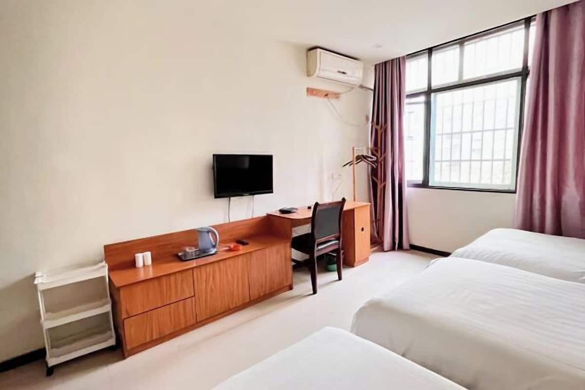 Quarto de hotel com cama, escrivaninha com cadeira, televisão e janela com cortinas.