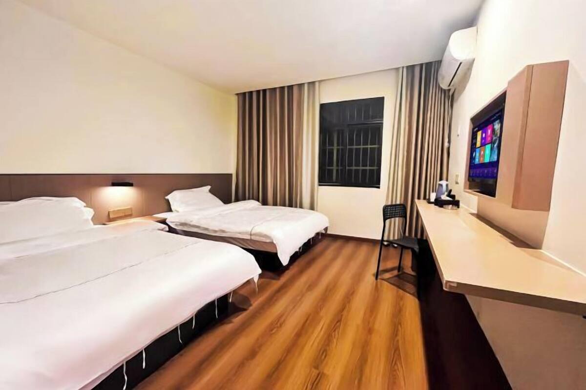 Quarto de hotel com duas camas, uma escrivaninha, uma cadeira, televisão e janela com cortinas.