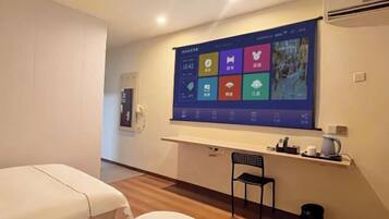 Habitación de hotel con una gran pantalla digital en la pared, un escritorio pequeño con una silla y dos camas.