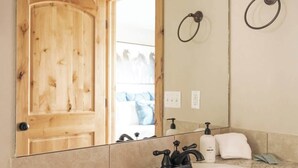 Un baño con puerta de madera, un lavamanos con grifo negro, un dispensador de jabón para manos y una toalla en la encimera.