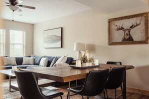 A modern living room with a wooden dining table, black chairs, a sofa with patterned cushions, a ceiling fan, and a framed deer picture on the wall. - 3 Bedrooms | Private Bathrooms | Rocky MTN Getaway (Fraser)