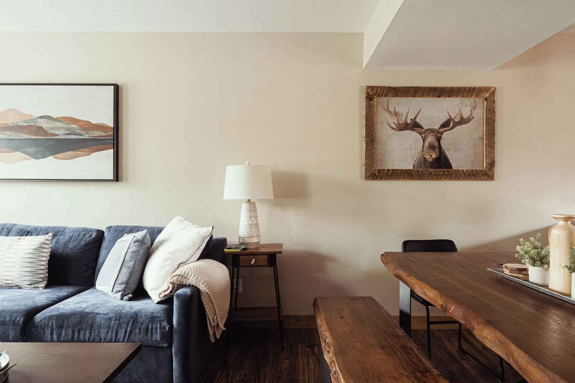 Een woonkamer met een bank, een tafel, een lamp en een lijst met een afbeelding van een eland.