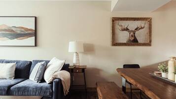 Een woonkamer met een bank, een tafel, een lamp en een lijst met een afbeelding van een eland.