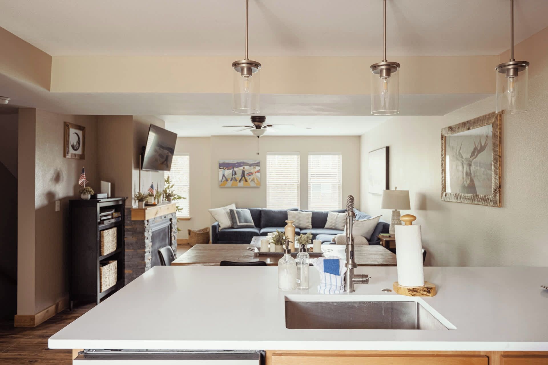 Een moderne keuken met een centraal eiland, een eethoek met een bank en een woonkamer met een televisie en kunstwerken.