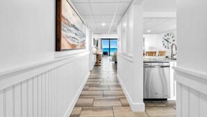 A hallway with a view to the outside, a kitchen area with a dishwasher, and a clock on the wall.