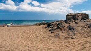 A sandy beach with rocky outcrops and a clear blue sky.