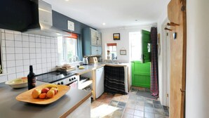 A modern kitchen with a stove, sink, and a wooden cutting board with fruits. - Y Cwtch, Newport - One Bedroom Cottage, Sleeps 2 (Newport)