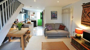 A living room with a sofa, a TV, and a lamp. There is a staircase leading to a kitchen. - Y Cwtch, Newport - One Bedroom Cottage, Sleeps 2 (Newport)