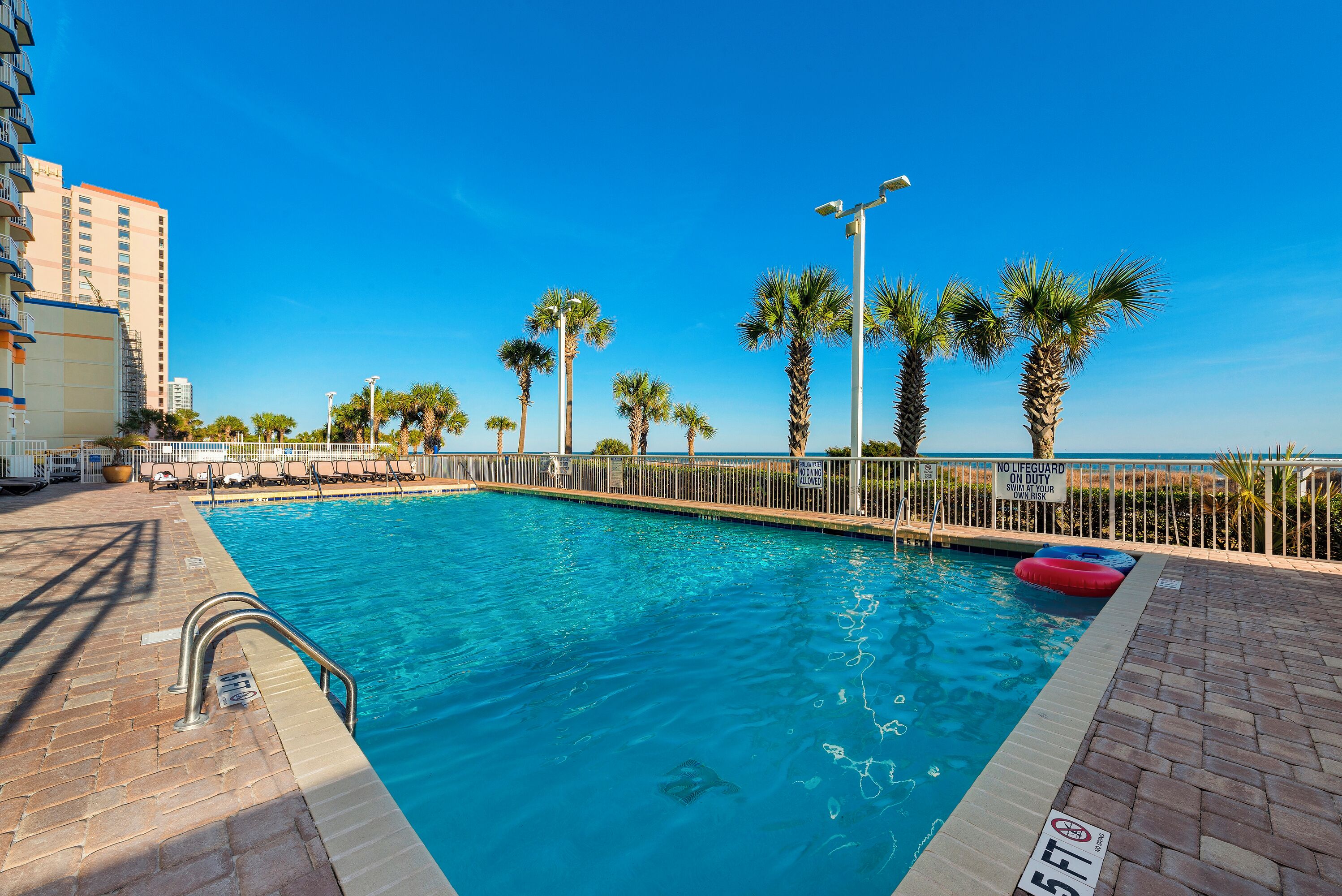 A swimming pool with a lifeguard stand, palm trees, and a clear blue sky.