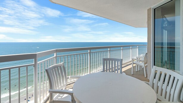 Un balcon avec vue sur l’océan, des chaises blanches et une table.
