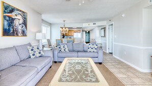 Un salon avec un canapé gris, un tapis à motifs, un ventilateur de plafond et un tableau représentant un oiseau.
