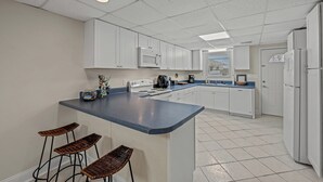 A modern kitchen with white cabinets, a blue countertop, and a central island with bar stools.