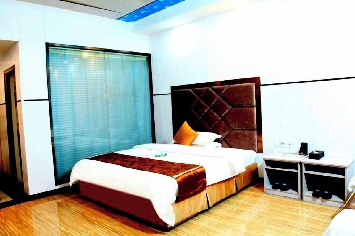 A hotel room with a large bed, a bedside table, a wardrobe, and a window with blinds.