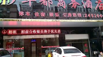 A hotel with a red signboard, a car parked in front, and a closed shutter door.