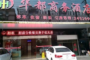 A hotel with a red signboard, a car parked in front, and a closed shutter door. - Huadu Business Hotel Chenzhou (Chenzhou)