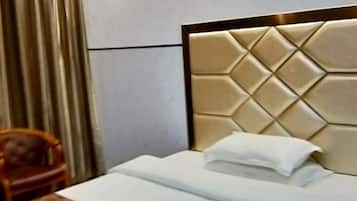 A neatly made bed with a padded headboard, a wooden chair, and a curtain in the background.