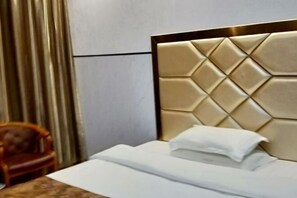 Una cama bien hecha con un cabecero acolchado, una silla de madera y una cortina al fondo.