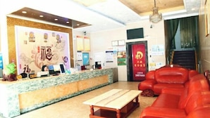 A hotel lobby with a reception desk, a red leather sofa, and a wooden coffee table. - Huadu Business Hotel Chenzhou (Chenzhou)