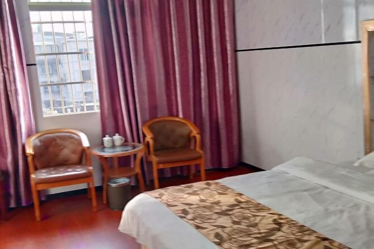 Habitación de hotel con cama, dos sillas de madera, una mesita redonda con tetera y una ventana con rejas.