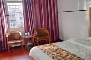 Habitación de hotel con cama, dos sillas de madera, una mesita redonda con tetera y una ventana con rejas.