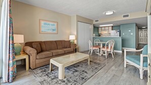 A living room with a sofa, coffee table, and chairs, a dining area with a table and chairs, and a kitchen area with a counter and appliances.