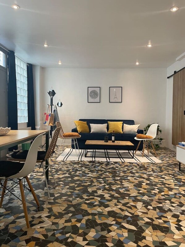 A modern living room with a sofa, dining table, chairs, and a patterned floor. - Luma Oberkampf Apartment / Jean Pierre Timbaud (Paris)