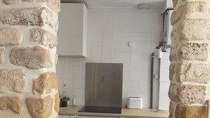 A kitchen with a stone wall, white cabinets, a stainless steel range hood, and a built-in oven. - Luma Oberkampf Apartment / Jean Pierre Timbaud (Paris)