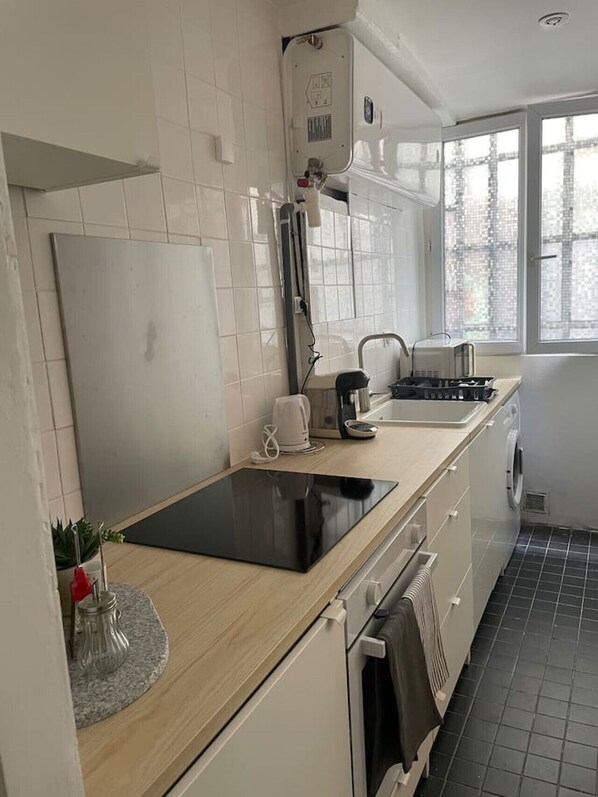A modern kitchen with a black countertop, white cabinets, a built-in oven, a coffee maker, and a window with a city view. - Luma Oberkampf Apartment / Jean Pierre Timbaud (Paris)