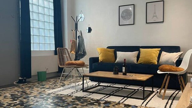 A modern living room with a patterned floor, a blue sofa with yellow cushions, a coffee table, and a chair. - Luma Oberkampf Apartment / Jean Pierre Timbaud (Paris)
