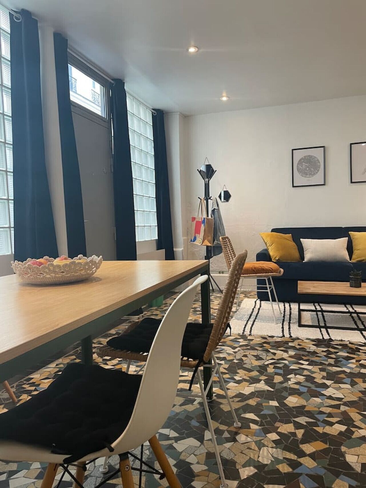Een eetgedeelte met een houten tafel, stoelen, een kamer met vloerbedekking, een bank met kussens en een raam met gordijnen.