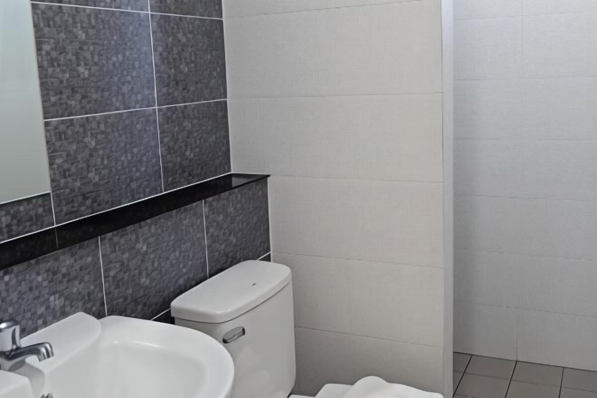 A bathroom with a white sink, a toilet, and a mirror above the sink. The walls are tiled in two shades of gray.