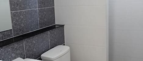 A bathroom with a white sink, a toilet, and a mirror above the sink. The walls are tiled in two shades of gray.