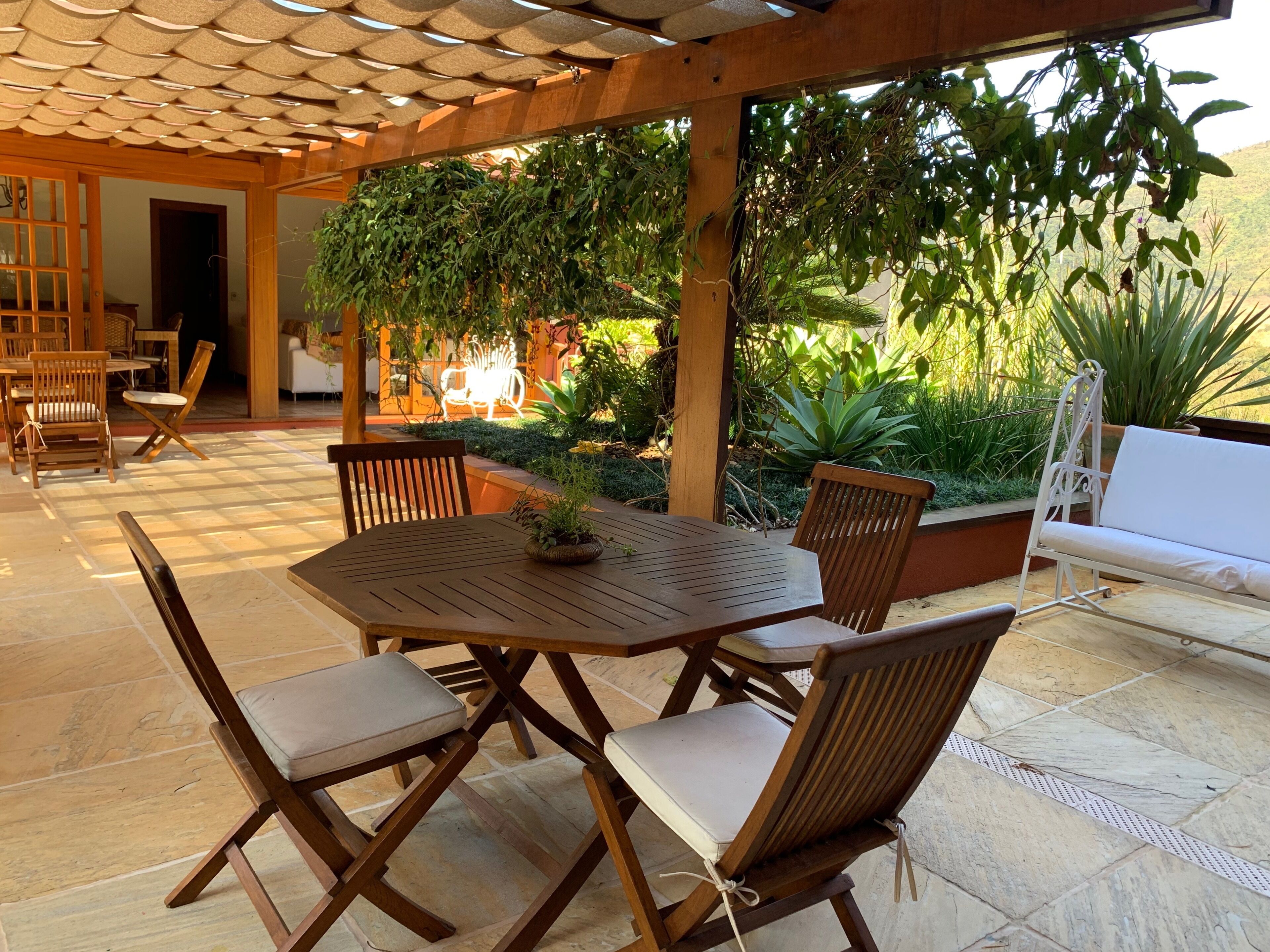 Une terrasse extérieure avec une table et des chaises en bois, entourée de verdure et agrémentée d’un canapé blanc.
