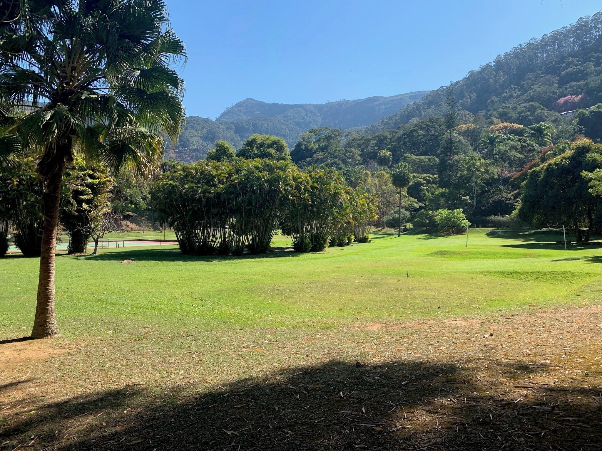 A golf course with a clear sky, lush greenery, and a hilly backdrop.