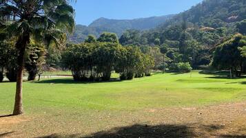A golf course with a clear sky, lush greenery, and a hilly backdrop.