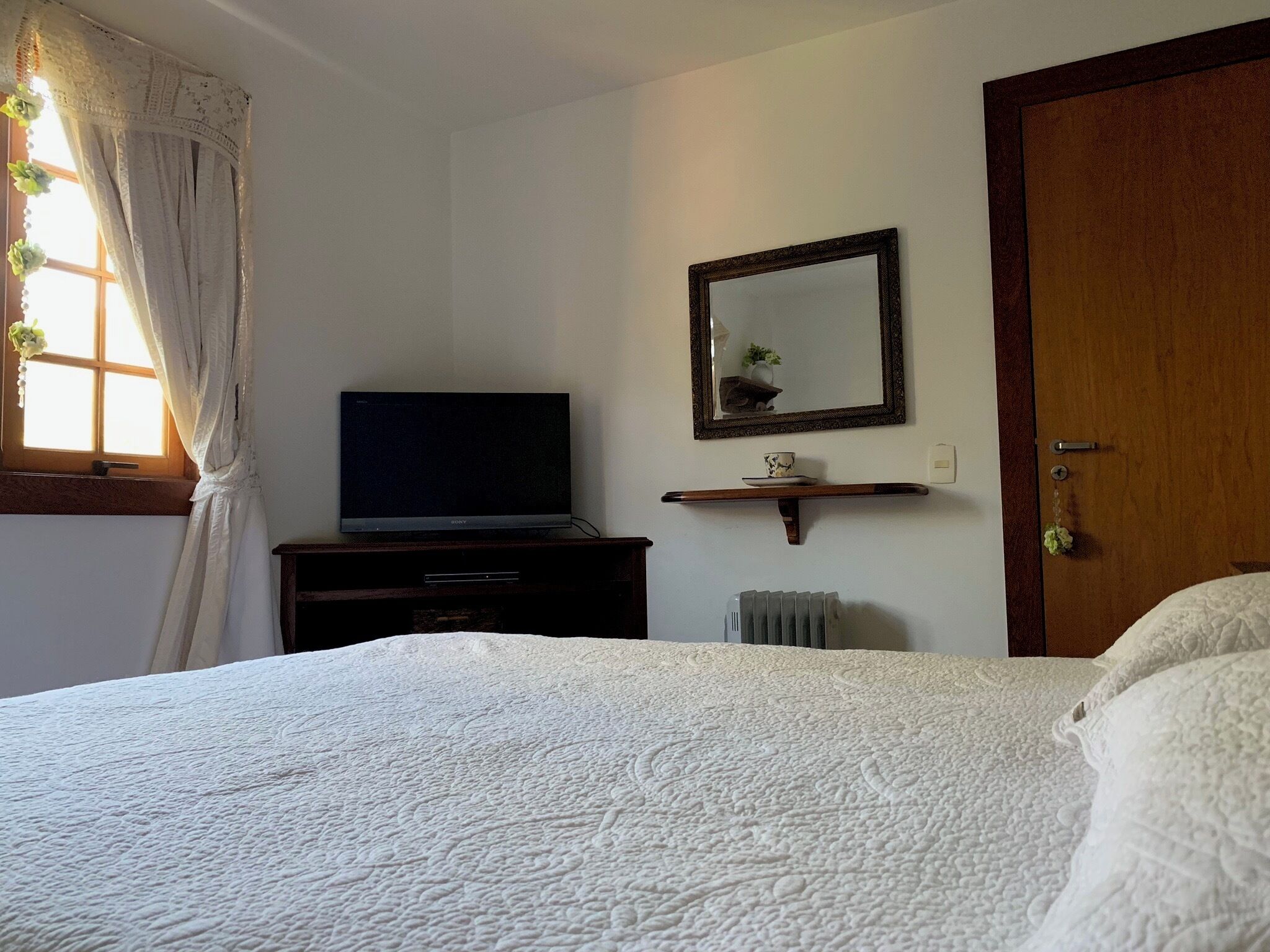 A bedroom with a bed, a television on a stand, a mirror, and a door.