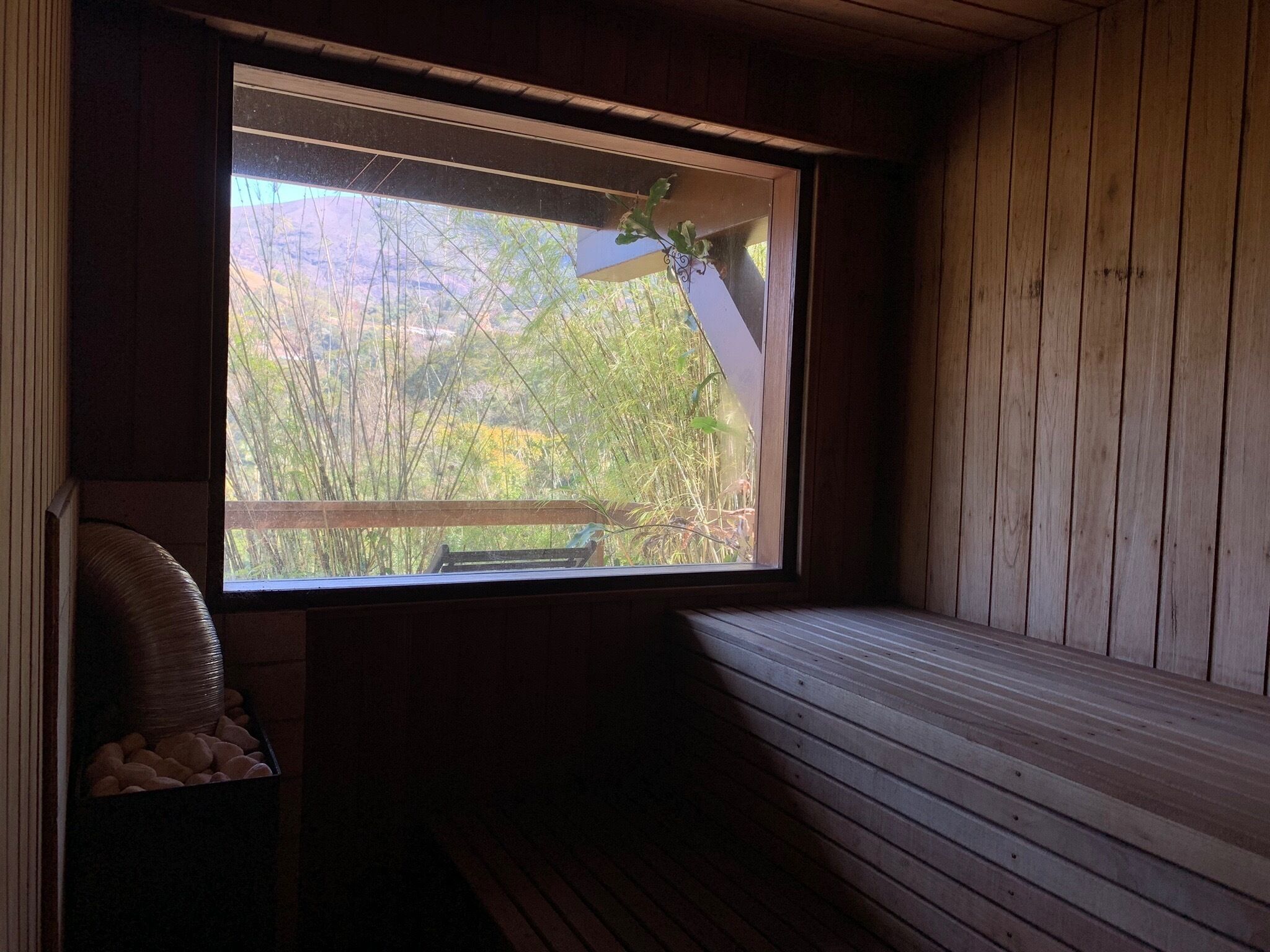 Une pièce avec un banc en bois, une fenêtre donnant sur un paysage verdoyant et un petit coin salon avec des coussins.