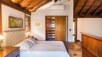 A bedroom with a large bed, wooden ceiling beams, a wooden wardrobe, and a framed picture on the wall.