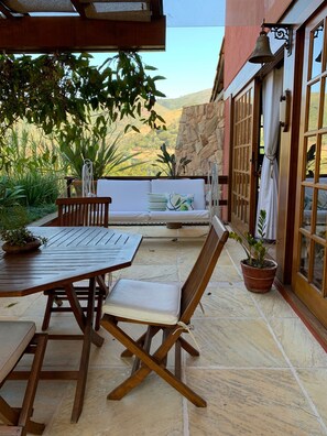 Eine Terrasse im Freien mit einem Holztisch, Stühlen, einer gepolsterten Bank und Blumentöpfen.