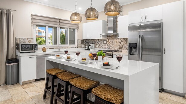 A modern kitchen with a central island, stainless steel appliances, and hanging pendant lights. - Amazing 4BR 3BA Villa Palm Beach w NEW Pool (Noord)