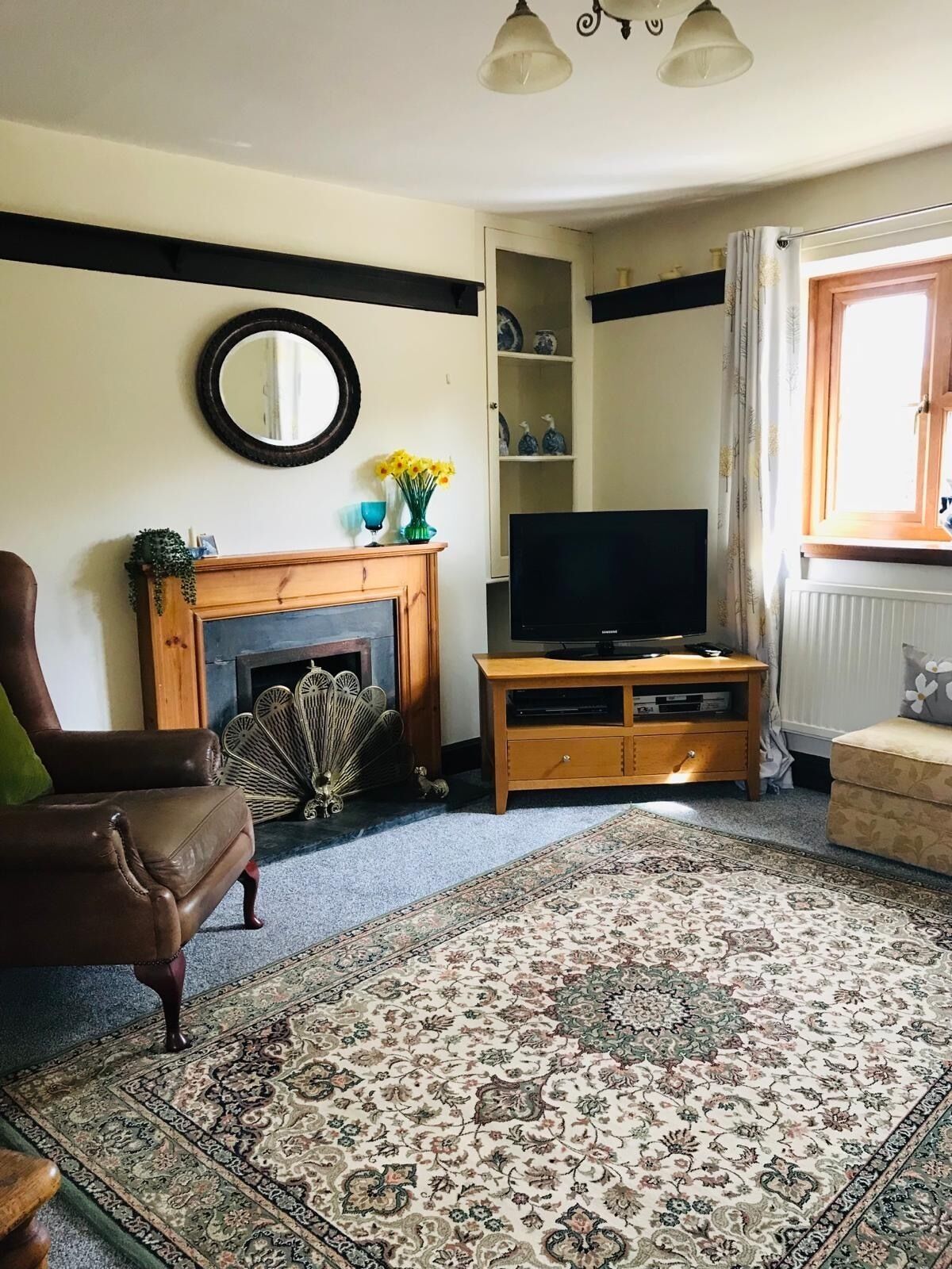 A living room with a fireplace, a television on a wooden stand, a brown leather sofa, and a patterned rug.