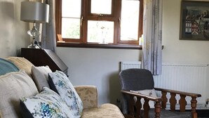 A cozy living room with a beige sofa, a wooden armchair, a small table, and a window with curtains. - Cozy country cottage in National Park  (Mamhilad)