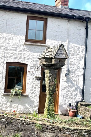 Una casa de piedra blanca con puerta de madera, una ventana pequeña y una chimenea de piedra.